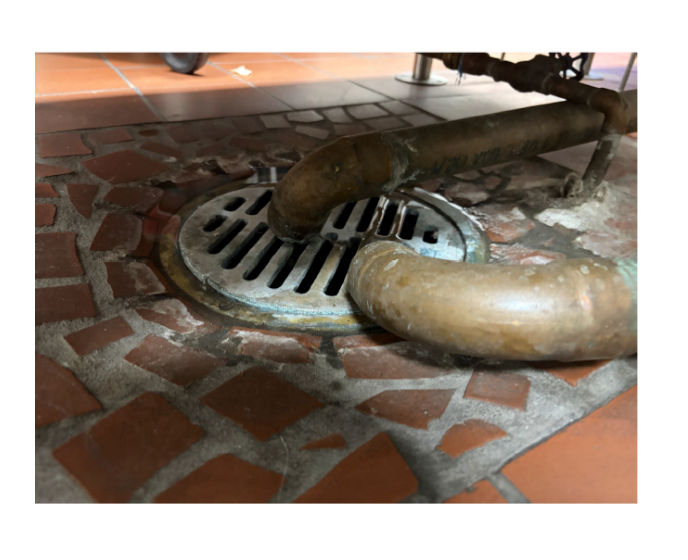 Photograph of a tiled floor with a deteriorated metal drain and kitchen surfaces at McKnight.