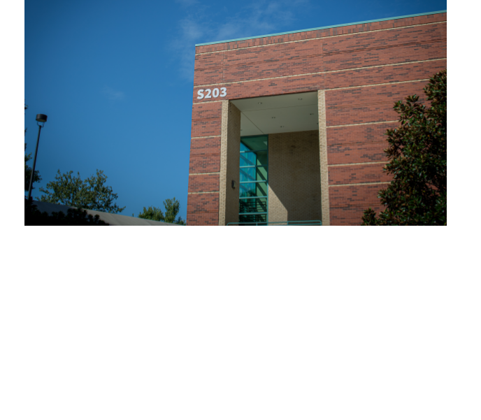 Photograph of a brick building exterior labeled S203 against a blue sky.